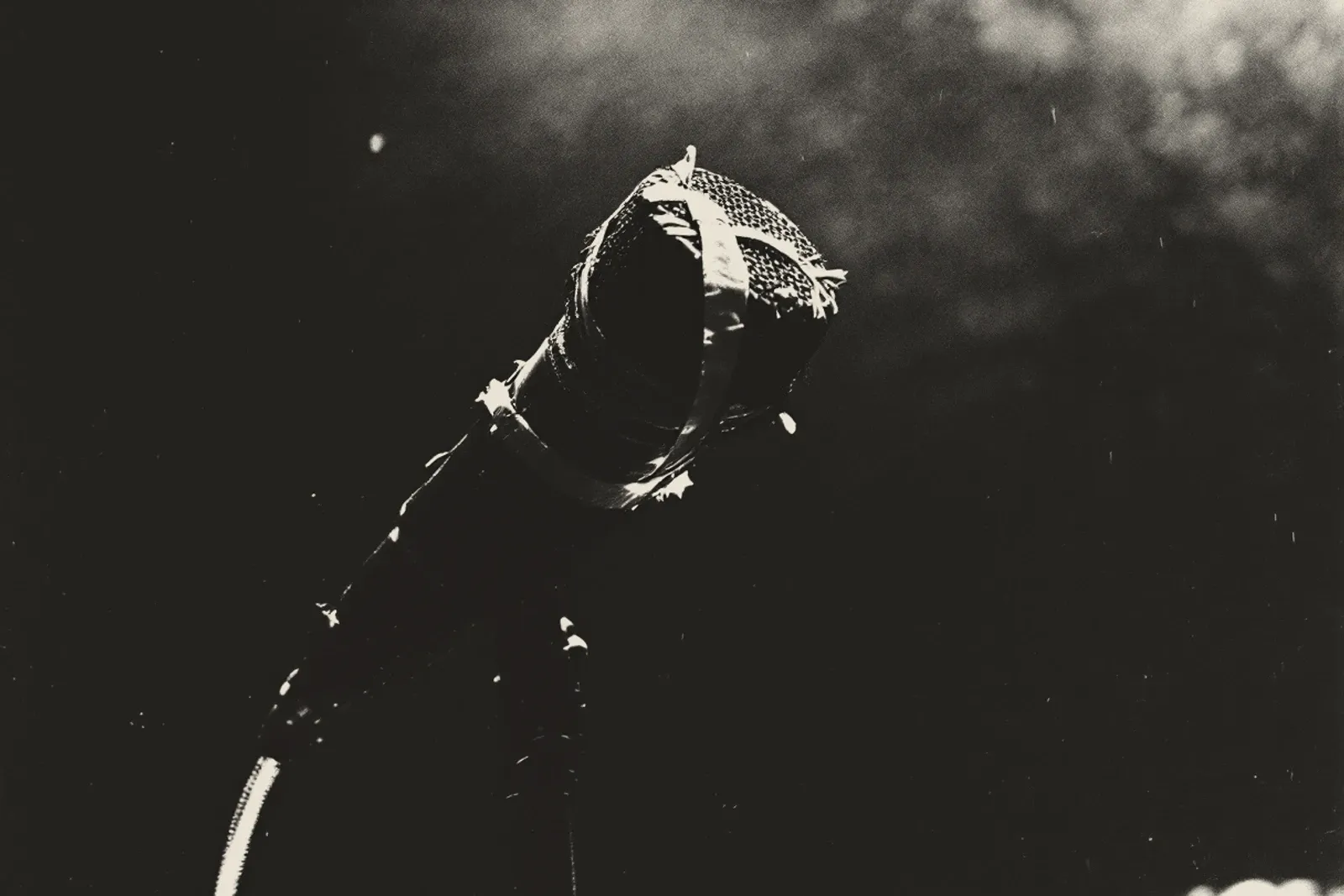 A dynamic microphone bound to its stand with tape, lit hard against a black stage, its lead falling away below.