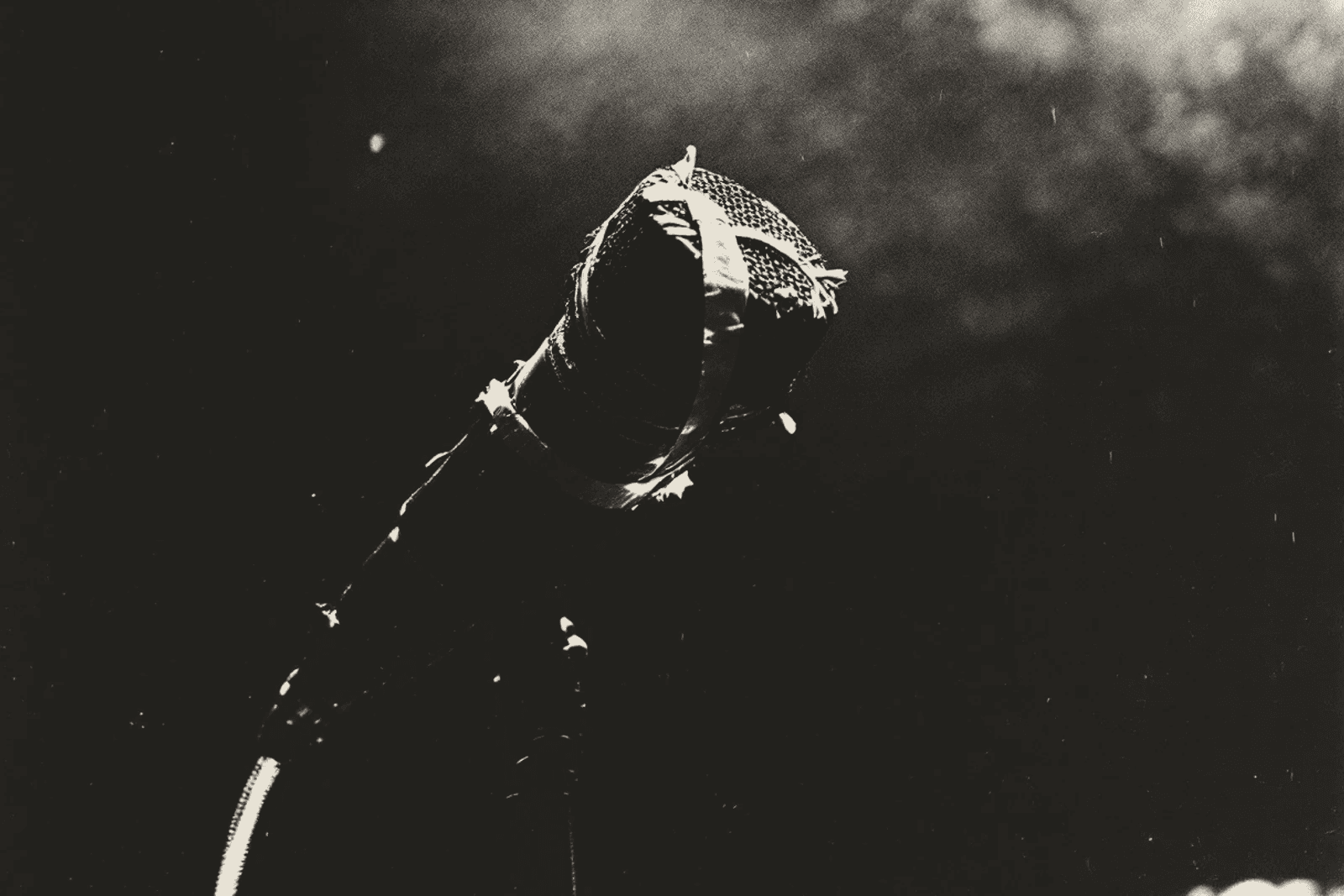 A dynamic microphone bound to its stand with tape, lit hard against a black stage, its lead falling away below.