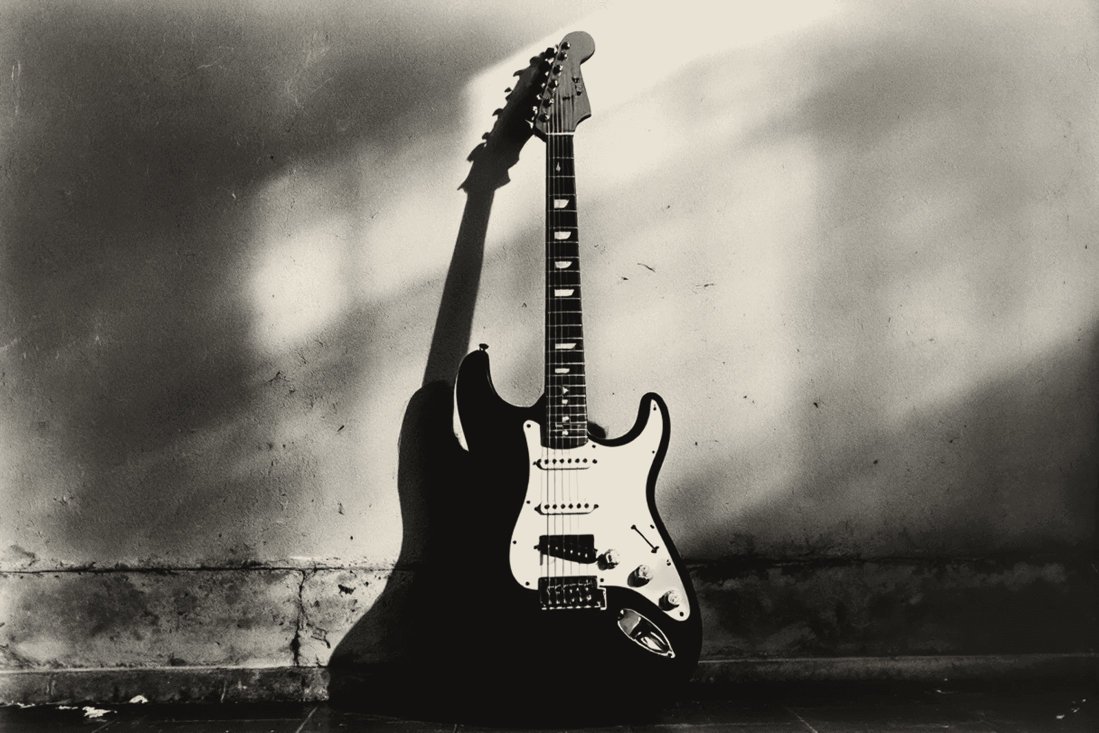 An electric guitar leaning against a bare wall in an empty room, raking light throwing its shadow across the plaster.